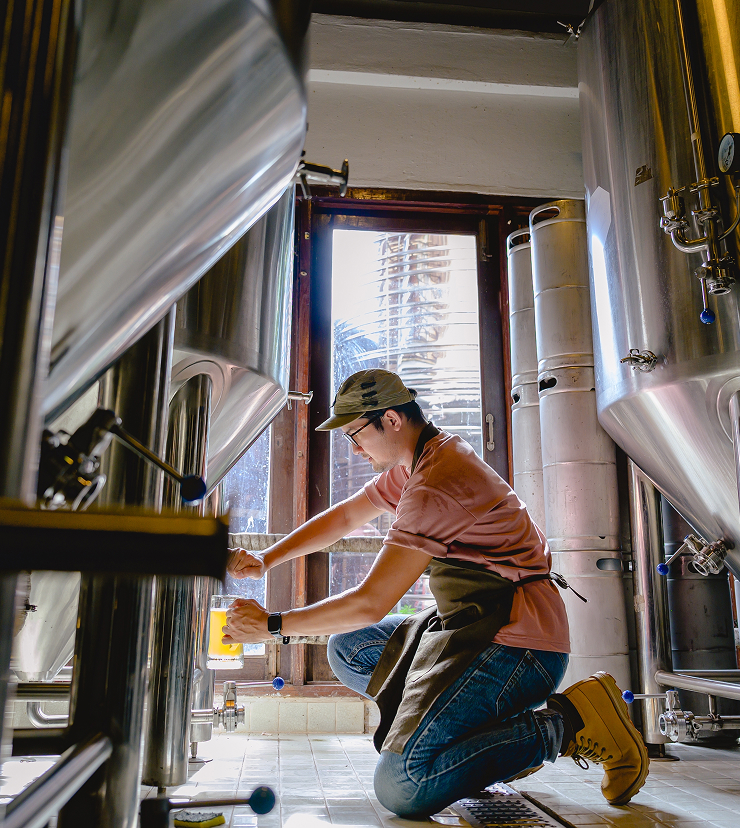 Brewer pouring beer from a vat into a glass.